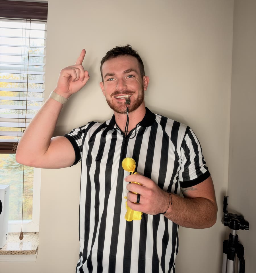 Evan Hand in a referee shirt, smiling and pointing up